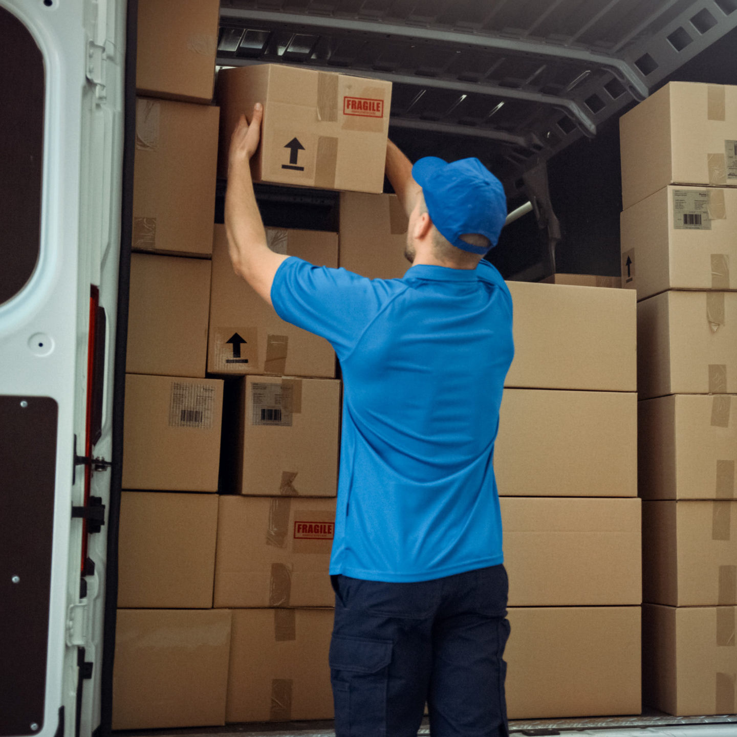 Courier Takes out Cardboard Box Package from Delivery Van Full of Parcels, Delivering Postal Parcel.